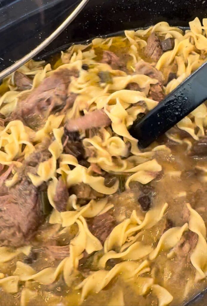 a bowl of Crockpot Beef Stroganoff with meat and a tongs