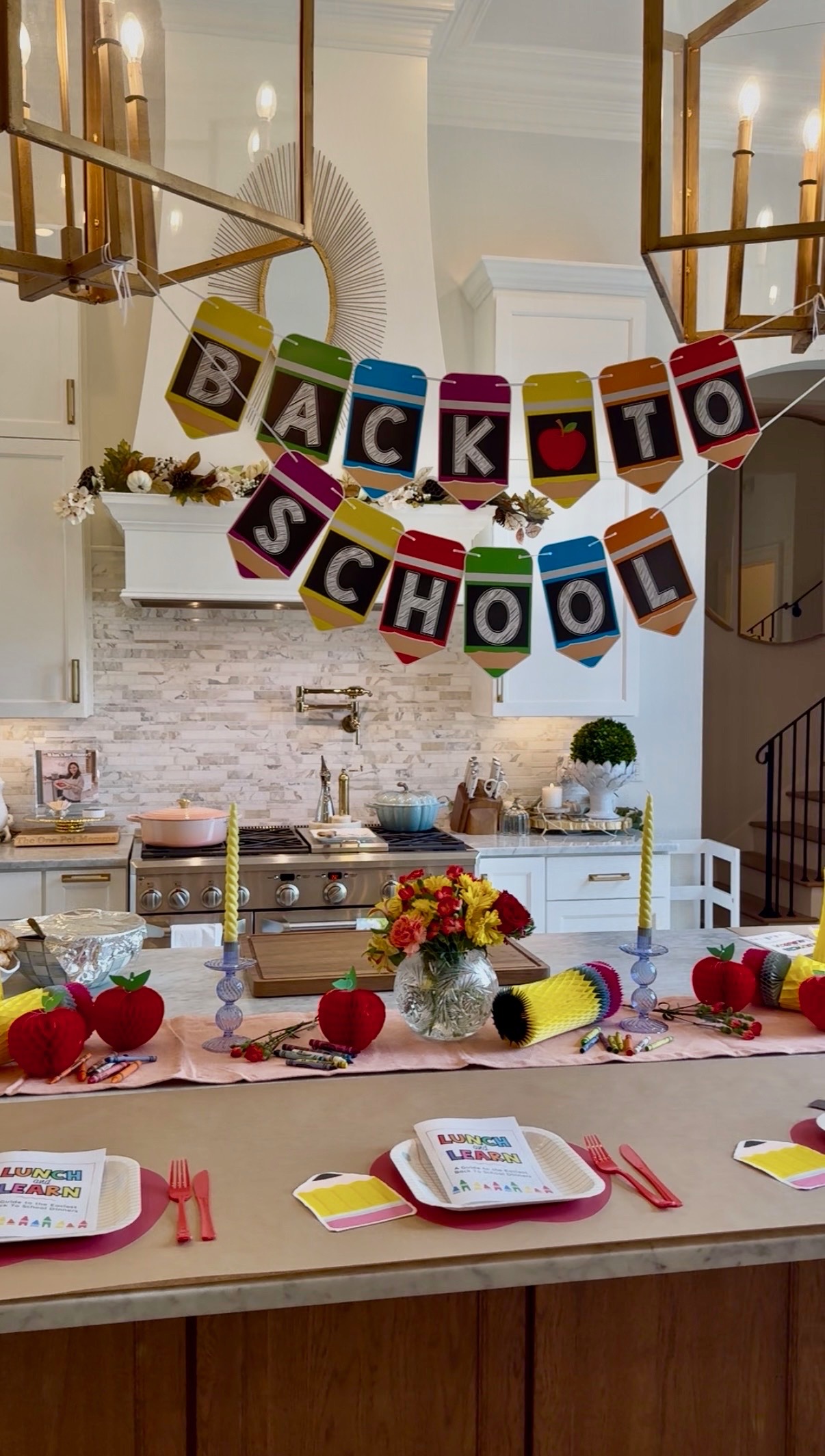 A kitchen decorated for a Back to School celebration, featuring a colorful banner, school-themed centerpieces, flowers, and table settings with themed plates, napkins, and red utensils—perfectly capturing the cheerful spirit that One Pot Momma brings to family gatherings.