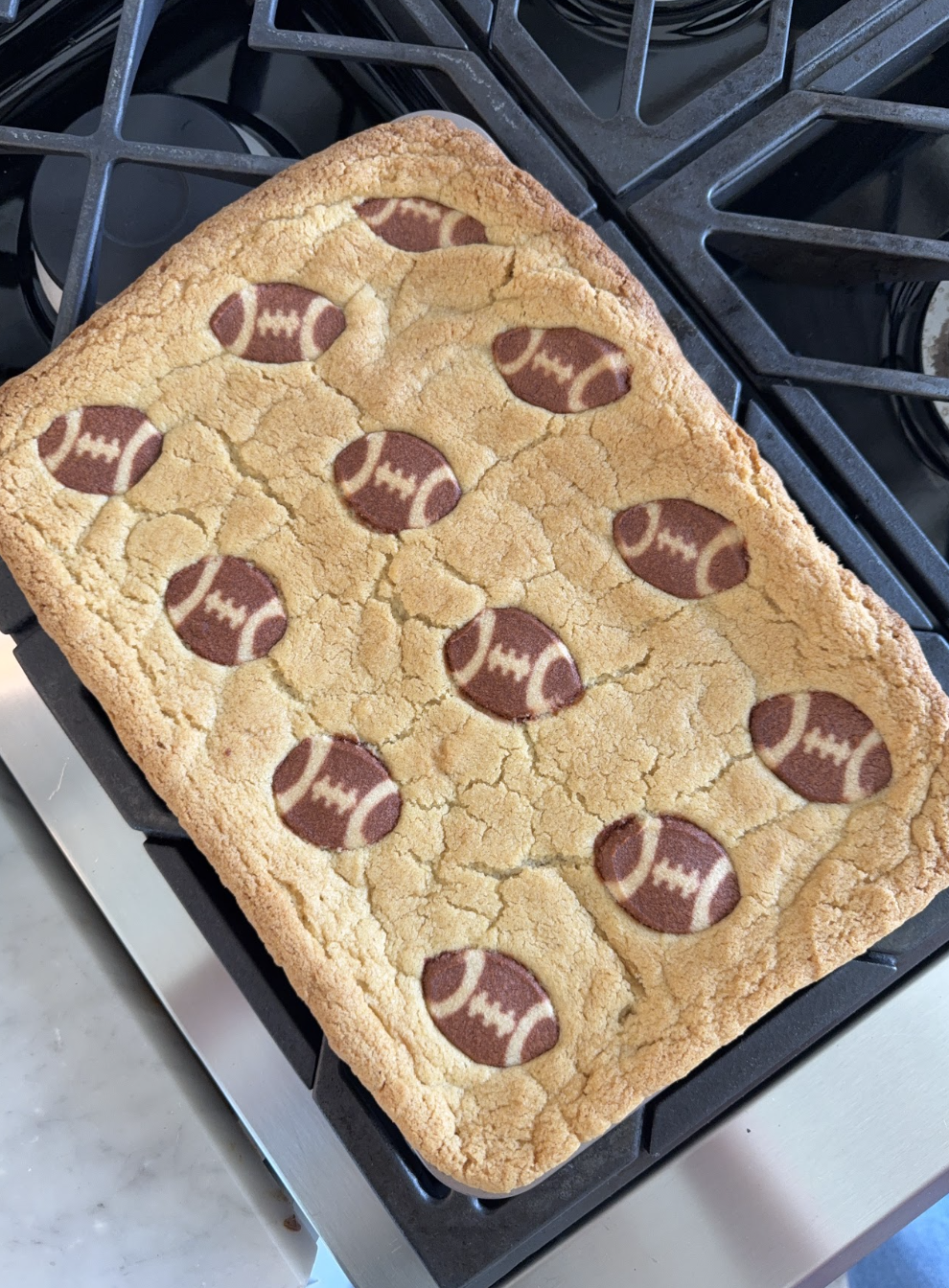 A large rectangular cookie with images of small footballs baked on top, resting on a stovetop.