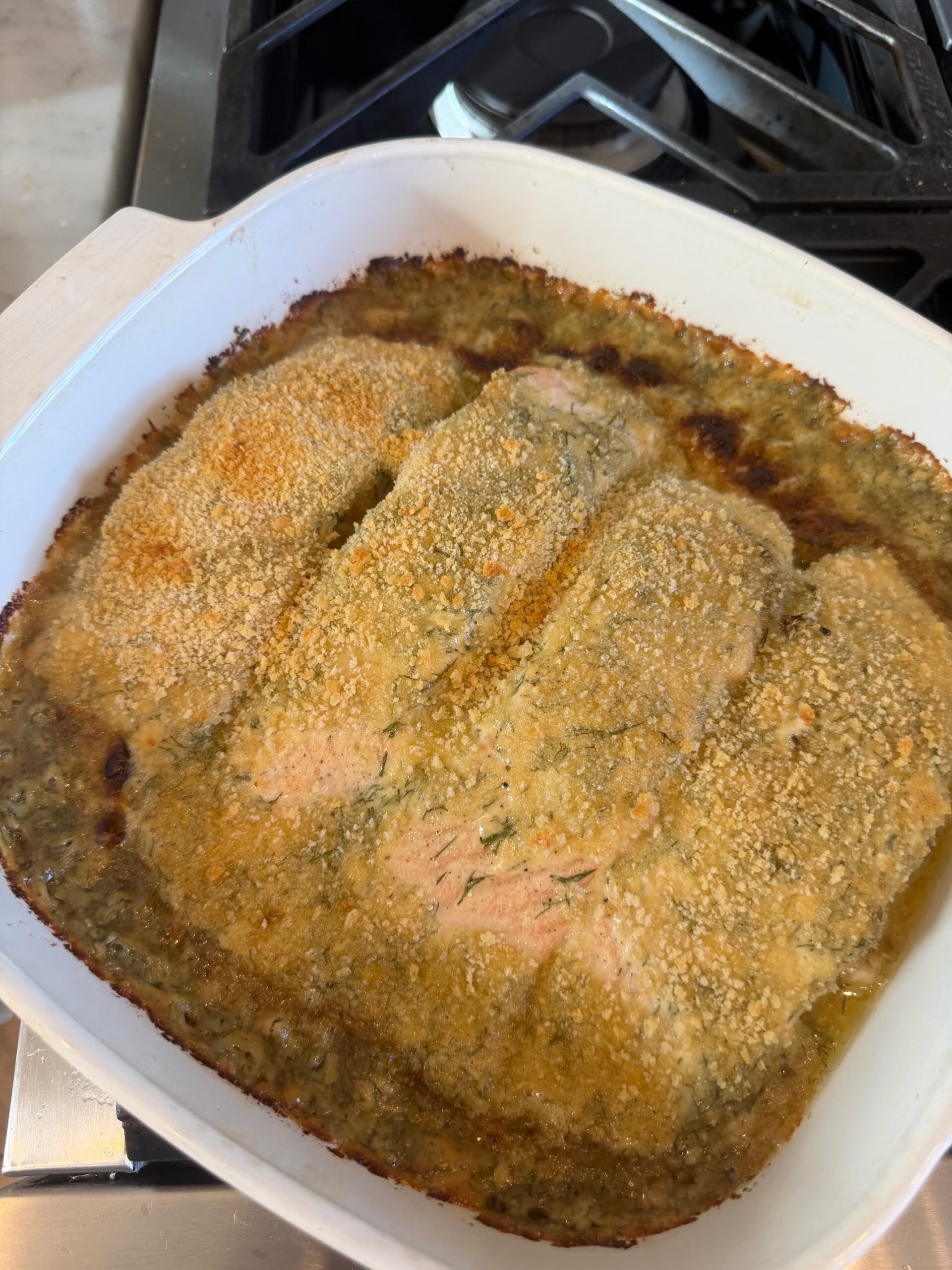 Baked lemon dill Parmesan salmon fillets topped with fresh dill in a white square baking dish.