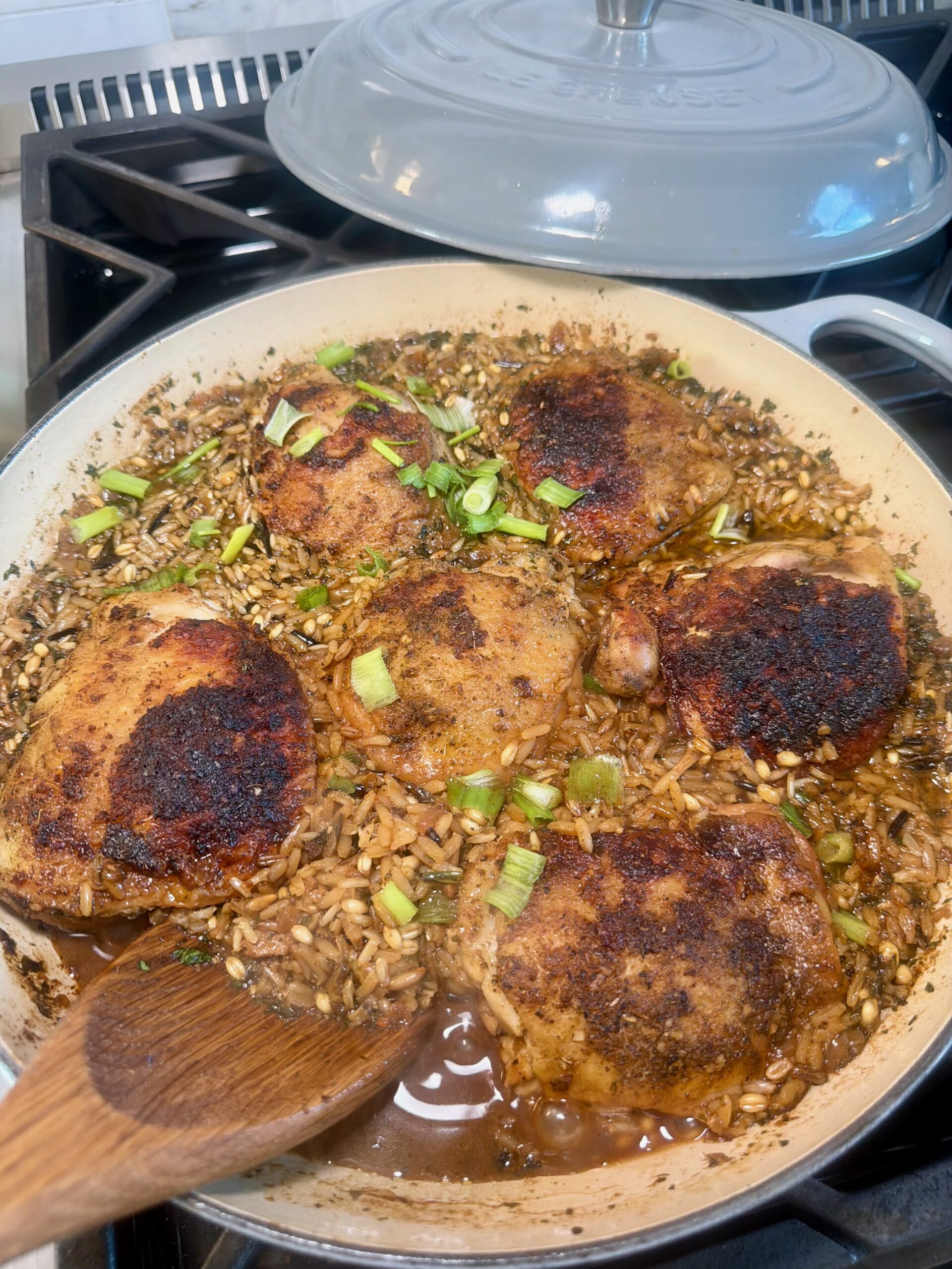 One-pot Cajun chicken and wild rice with crispy seared chicken thighs and chopped green onions in a braiser.