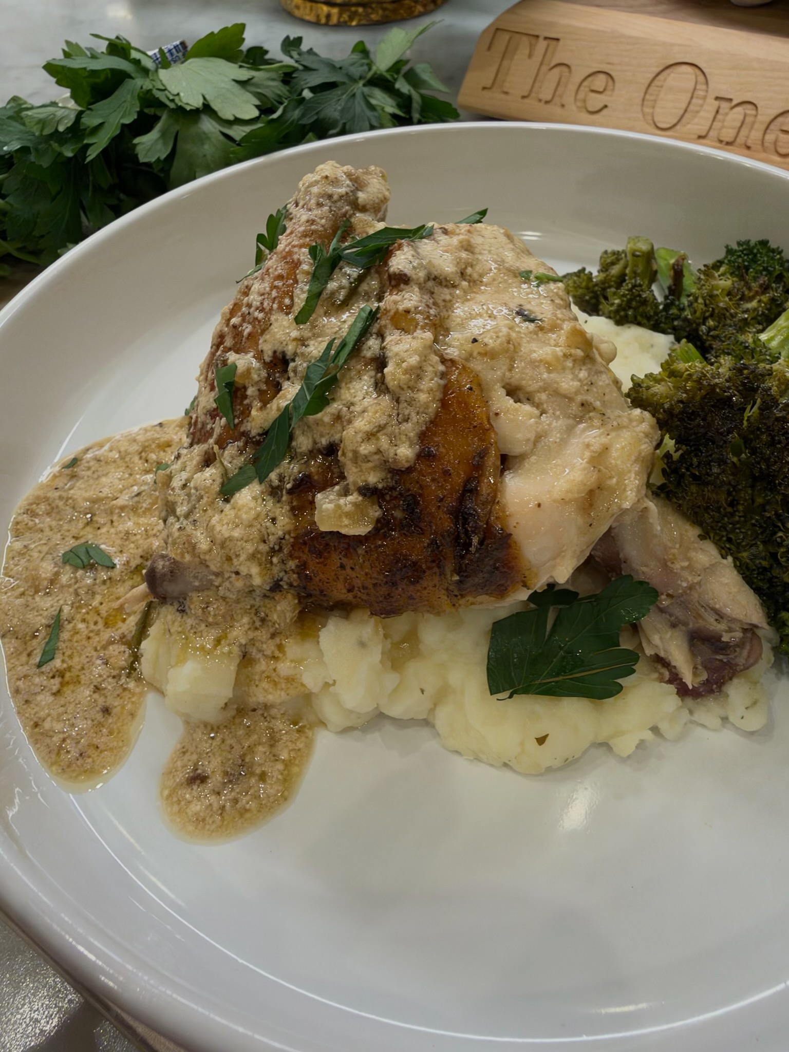 A plate of spatchcock chicken au poivre over mashed potatoes, topped with creamy au poivre sauce, with roasted broccoli on the side.