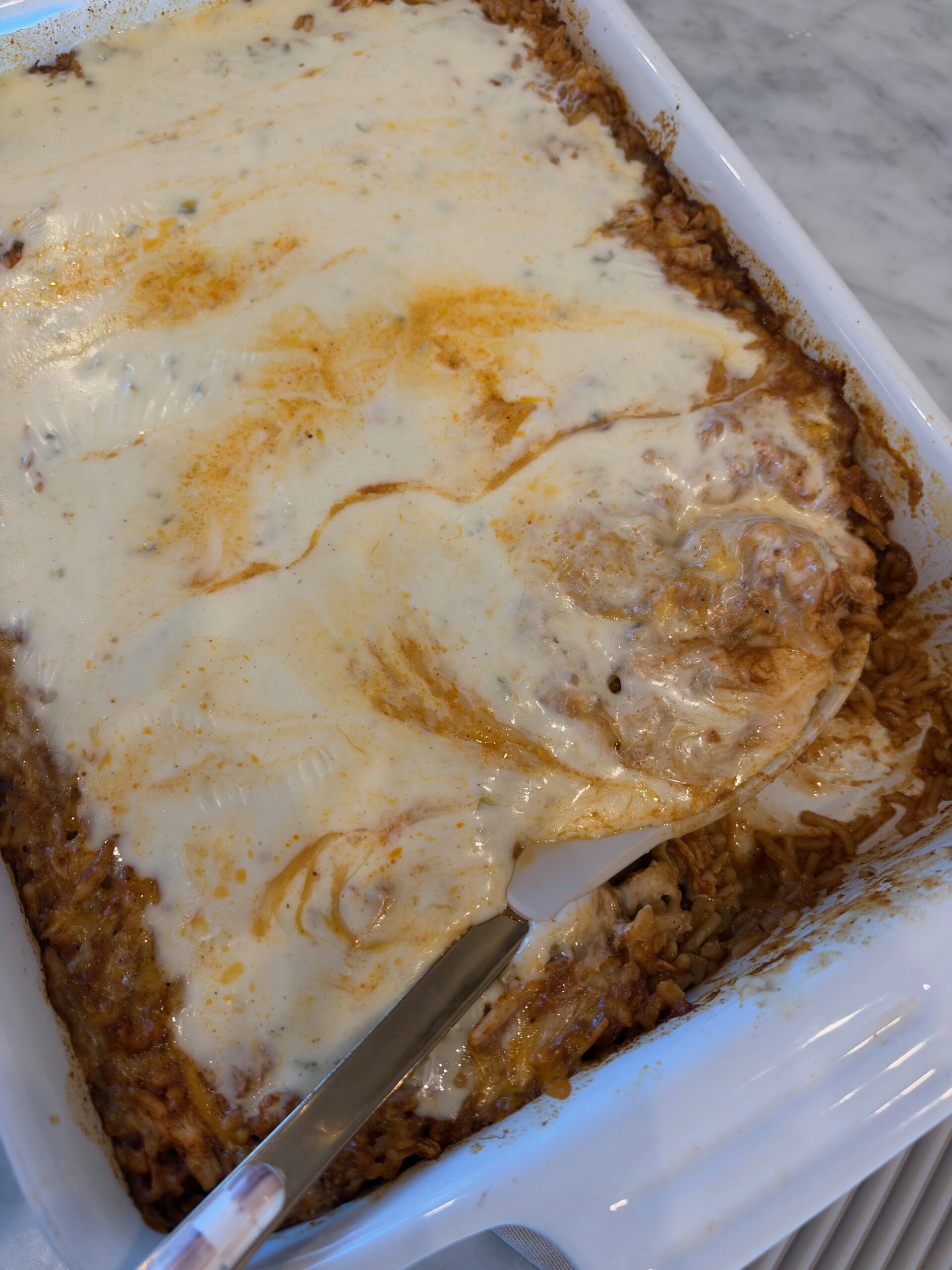 Swim queso chicken taco rice casserole in a white baking dish, covered in melted cheese and warm queso.
