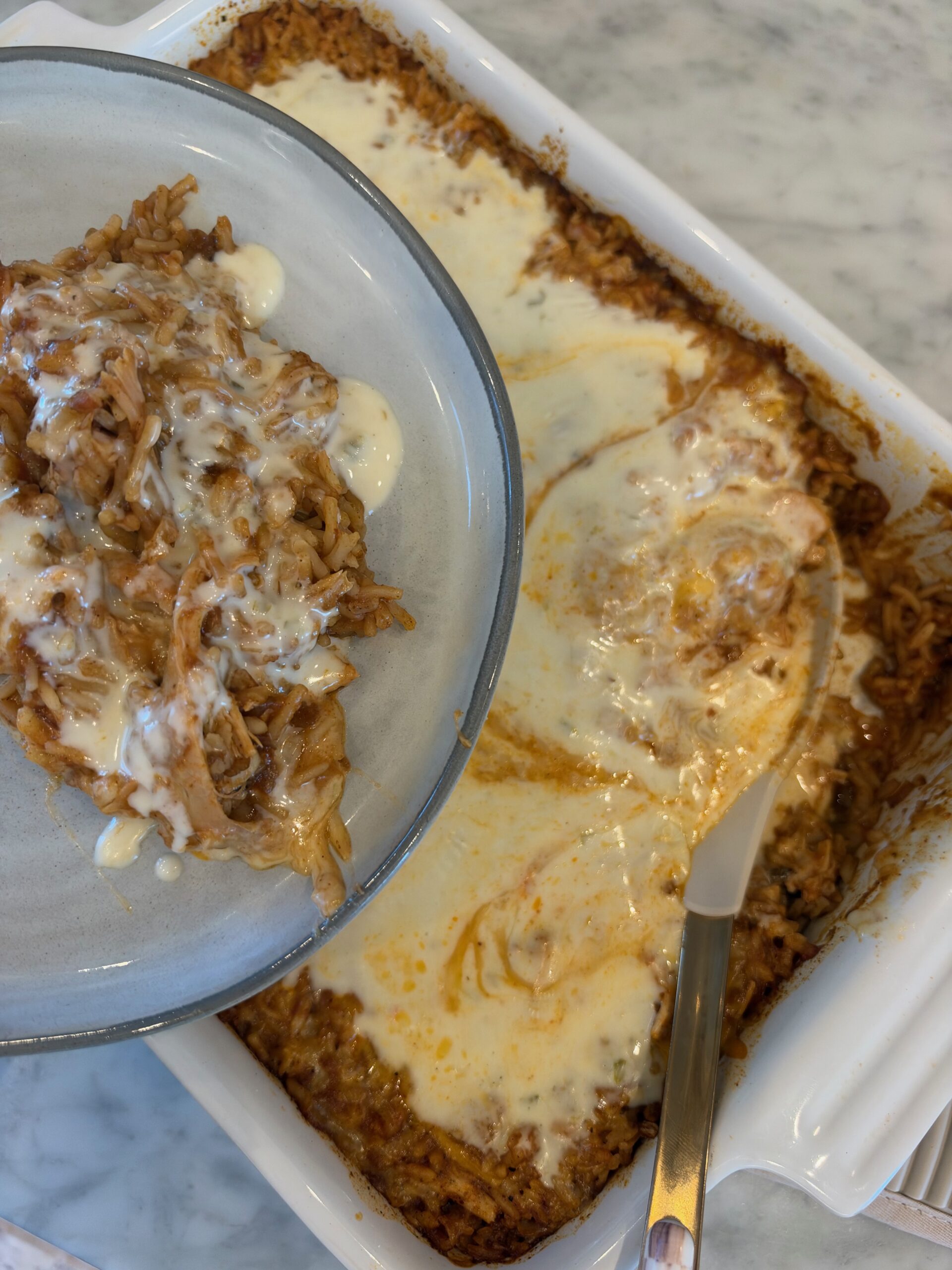 A plate of cheesy queso chicken and rice casserole held over the baking dish.